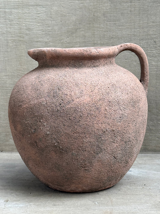 Jarrón de terracota sin esmaltar con asa, cuerpo panzudo, sobre fondo de hormigón