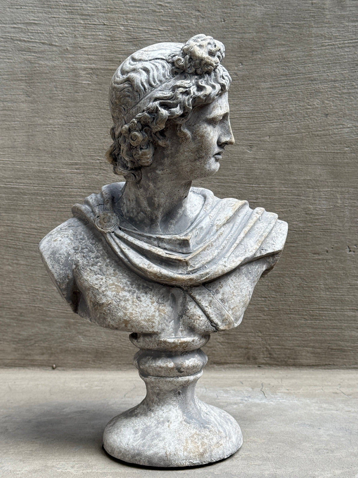Busto de Apolo decorativo en tono gris piedra, sobre fondo de hormigón