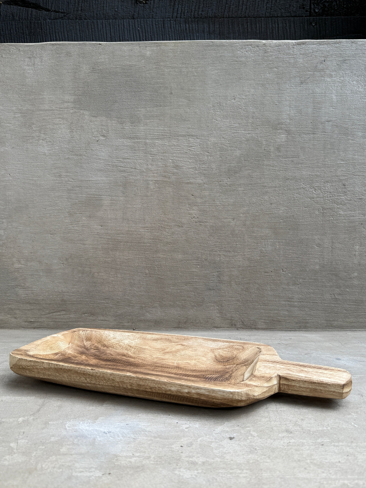 Tabla de madera tallada con mango, sobre fondo de hormigón