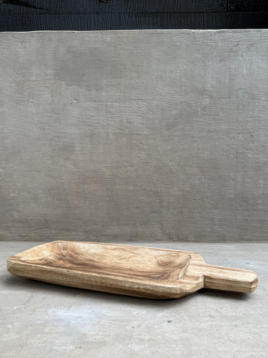 Tabla de madera tallada con mango, sobre fondo de hormigón