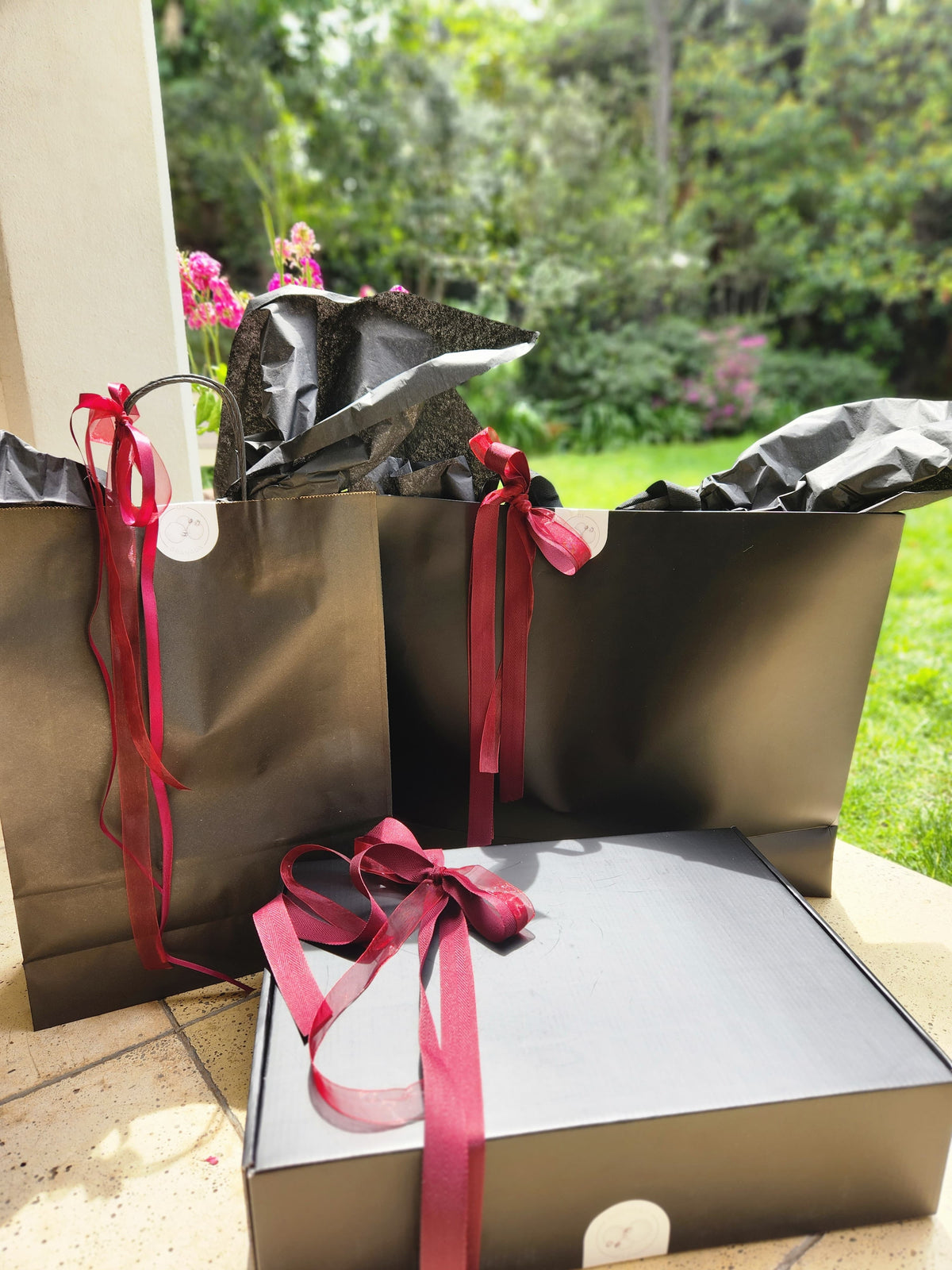 Bolsa y caja de regalo de De Granada Deco, envueltas con cintas granate